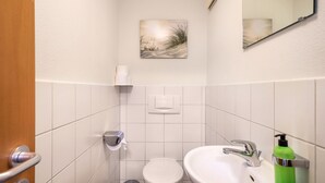 Casa de banho com sanita, lavatório e um quadro na parede.