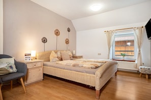 Une chambre à coucher comprenant un lit, une table de chevet, une lampe, une chaise, une fenêtre avec des rideaux et un téléviseur.