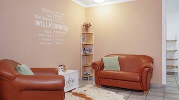 Ein Zimmer mit zwei Ledersofas, einem Couchtisch, einem Bücherregal und einer Wand mit mehrsprachigem Willkommenstext.