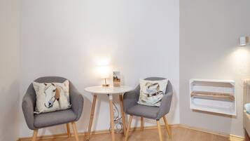 Två grå fåtöljer med kuddar prydda med hästmotiv, ett litet runt bord med en lampa och en bok, och en vit hylla som står mot en enkel vägg.