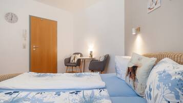 Ein Schlafzimmer mit einem Bett, einer Holztür, einem kleinen Tisch mit Stühlen und einer Wanduhr.