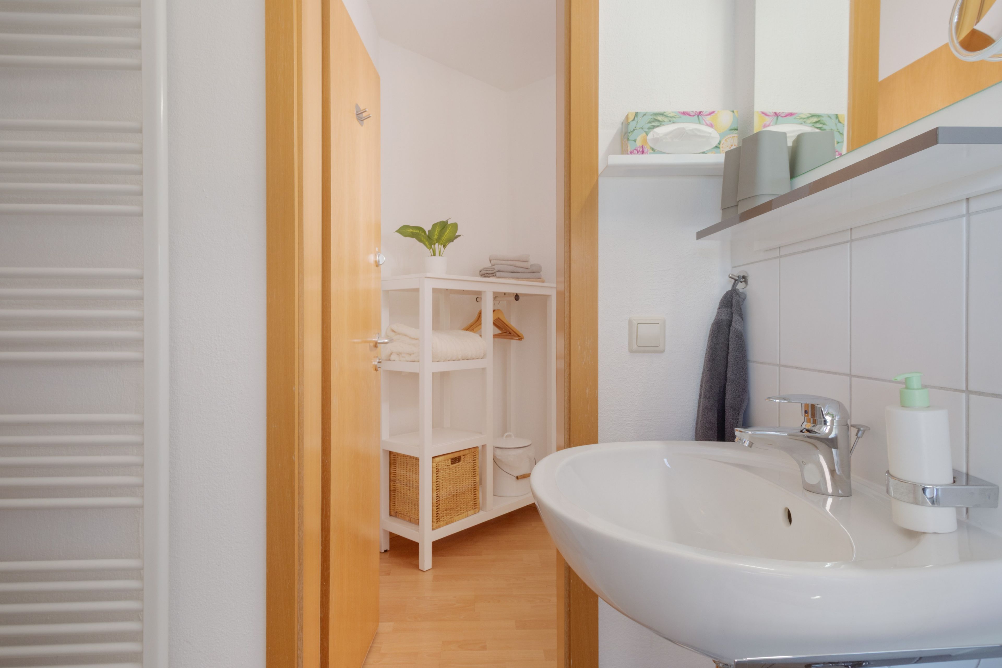 Ein Badezimmer mit einem weißen Waschbecken, einem Spiegel und einem Ablagefach mit Pflegeprodukten.
