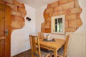 A dining area with a stone wall, wooden table, chairs, and a window. - Apartment 'Ferienhäuschen' with Private Terrace, Shared Garden and Wi-Fi (Ravensburg)