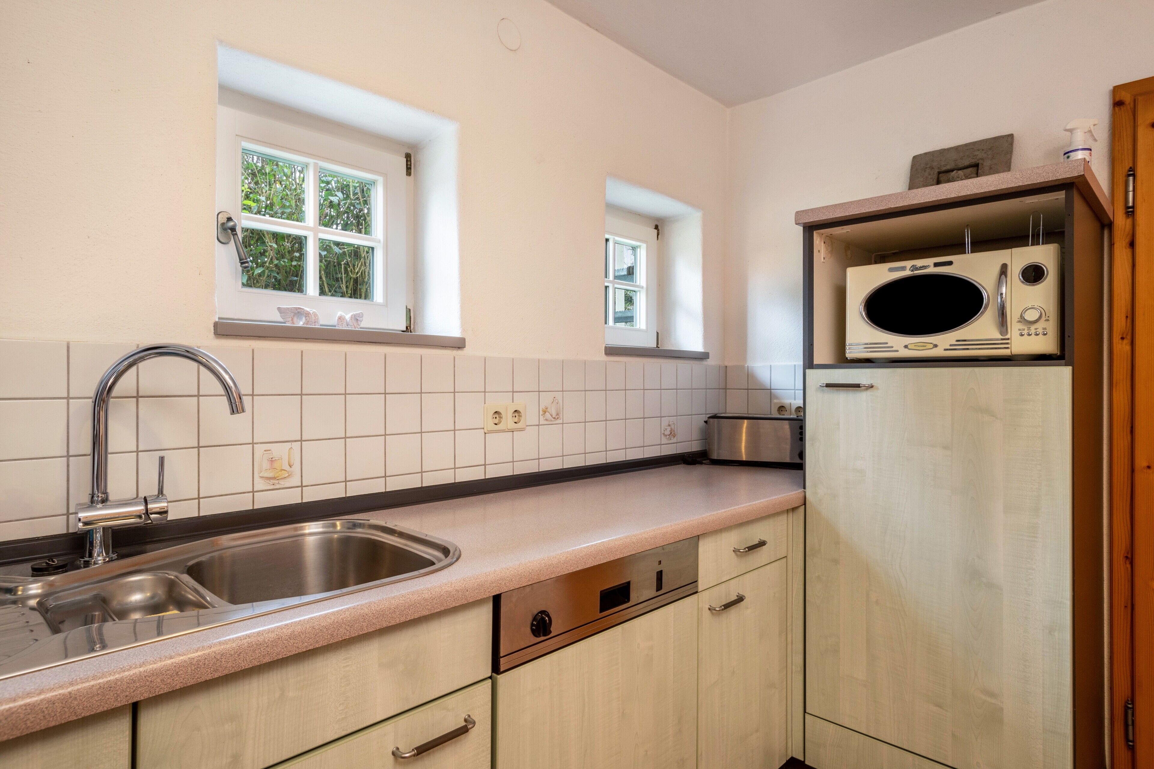 Eine Küche mit Spüle aus Edelstahl, Holzschränken, einer Mikrowelle und einem Fenster.