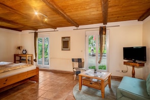 A room with a wooden ceiling, a bed, a TV, a table, a chair, and a view through a door. - Apartment 'Ferienhäuschen' with Private Terrace, Shared Garden and Wi-Fi (Ravensburg)