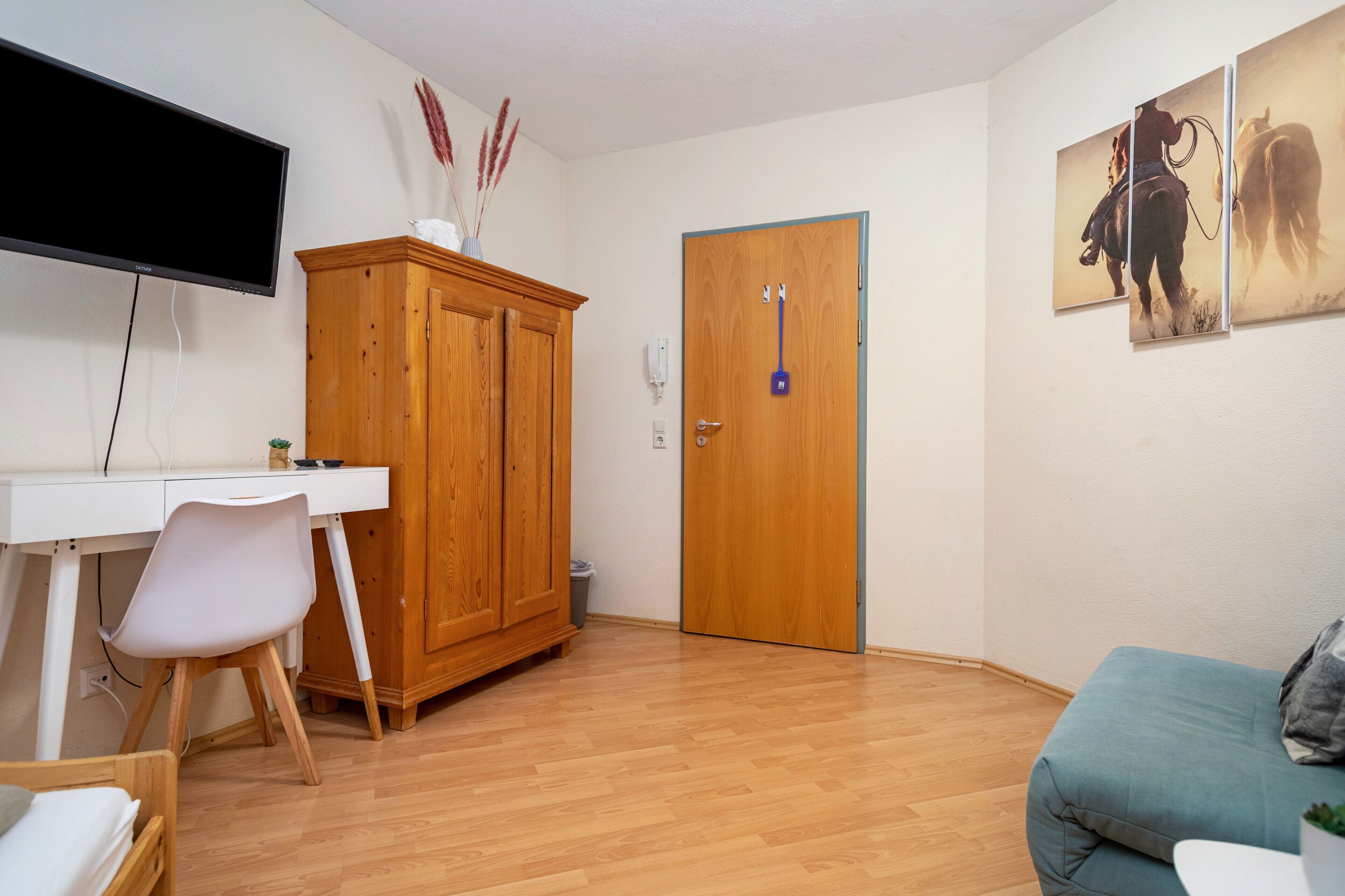 Una habitación con un armario de madera, un escritorio, una silla, un televisor, una puerta y un sofá.