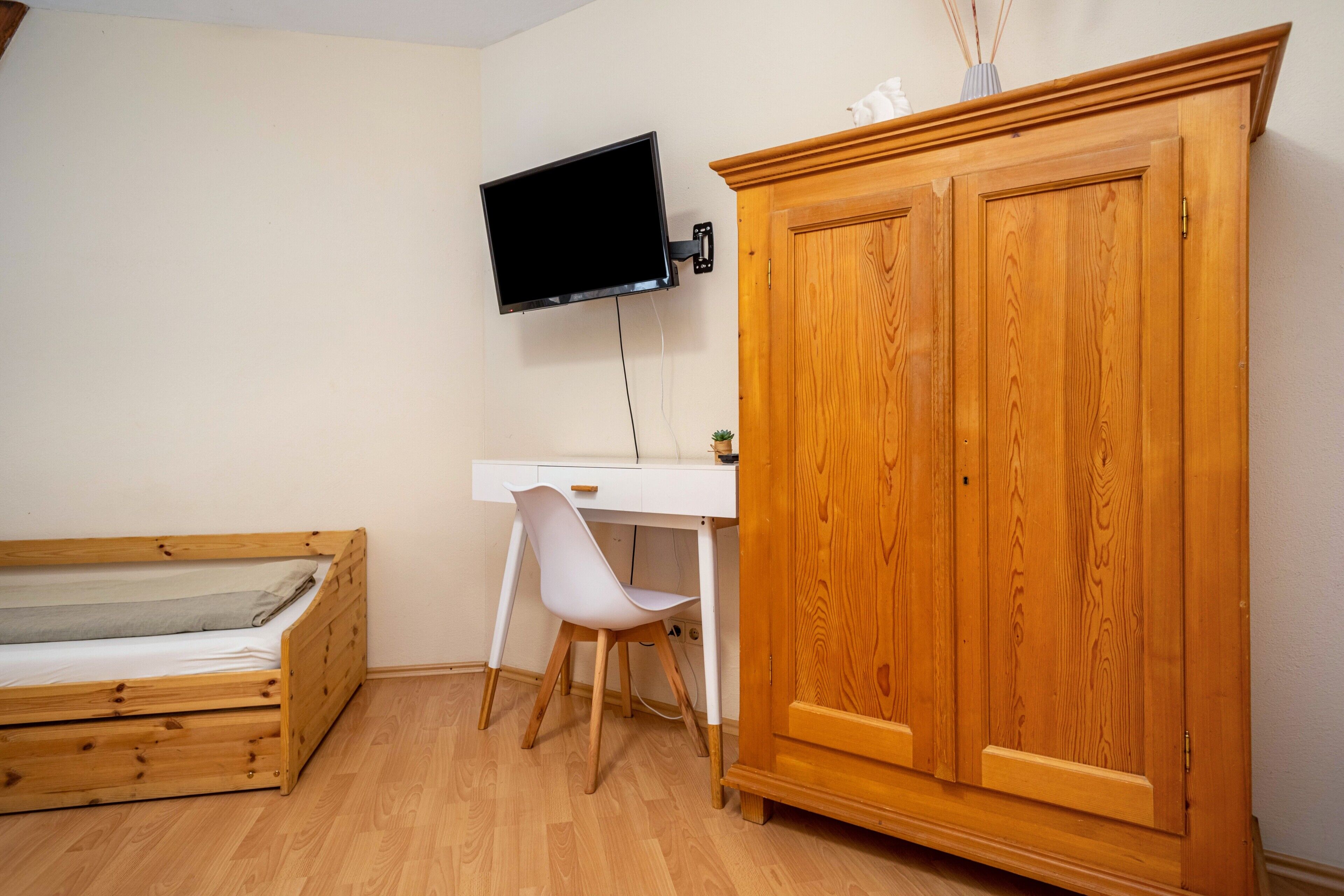 Une pièce comprenant une armoire en bois, un bureau avec une chaise, un lit et un téléviseur fixé au mur.