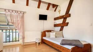 Un dormitorio con una cama de madera, un televisor montado en la pared, una ventana con cortina y un radiador.