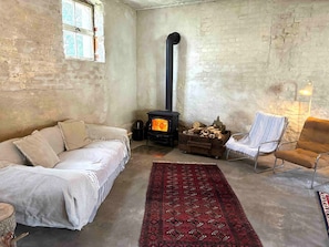 Una habitación acogedora con una cama, una silla, un tapete, una chimenea y una ventana.