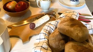 Ein Esstisch mit Kerze, Obstschale, Brot und einer Vase mit Blumen.