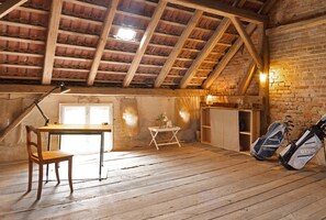 Una habitación rústica con techo de madera, un escritorio, una silla, una mesita con una lámpara y bultos de golf.
