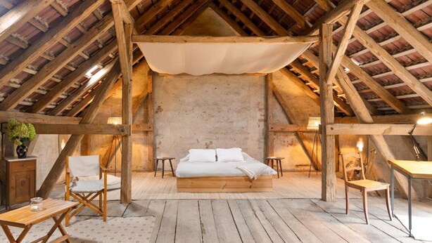 Ein Schlafzimmer im Dachgeschoss mit Holzbalkendecke, einem Bett, zwei Stühlen, einem kleinen Tisch und einer Lampe.