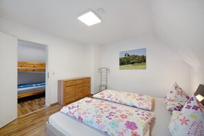 Een slaapkamer met stapelbedden, een houten dressoir, een kleine trap en een lijst met een foto aan de muur.