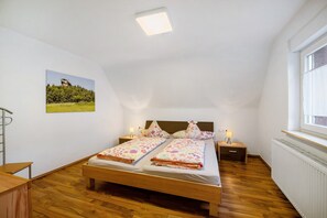 Un dormitorio con una cama de madera, dos mesitas de noche con lámparas, un ventanal y un cuadro en la pared.