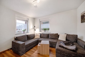 A modern living room with a sectional sofa, a wooden coffee table, and two windows with curtains.
