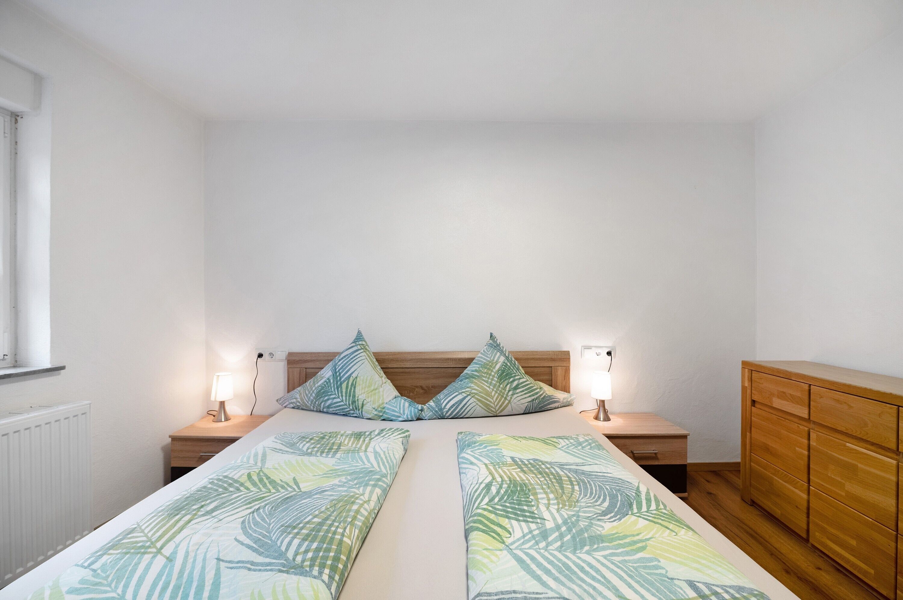 Une chambre à coucher comprenant un lit, deux lampes de chevet, une tête de lit en bois, une table de chevet et une commode en bois.