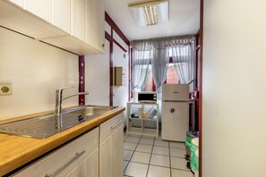 Une cuisine compacte dotée d’un évier en acier inoxydable, d’un plan de travail en bois, de meubles blancs, d’un four à micro-ondes et d’un réfrigérateur.