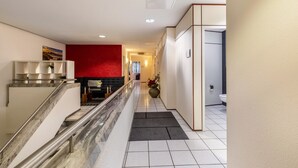Ein Hotel-Flur mit einer Marmortreppe, einer roten Akzentwand, einem Empfangsbereich und einem Badezimmer mit Toilette.