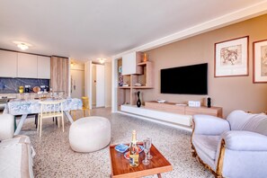 A modern living room with a flat-screen TV, a sofa, a dining area with a table set for two, and a kitchen in the background. - Rives d'Azur Apt with Sea View Terrace, Menton, France (Menton)
