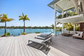 A wooden deck with lounge chairs, a sofa, and a glass balustrade overlooking a marina with boats. - Riverside Elegance on Noosa Parade (Noosa)