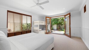 A bedroom with a bed, a ceiling fan, a window with blinds, and an open door leading to a balcony with plants. - Riverside Elegance on Noosa Parade (Noosa)