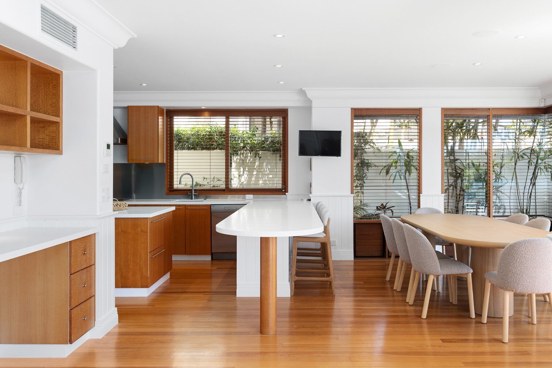 Una cocina moderna con armarios de madera, encimera blanca y comedor con mesa y sillas.