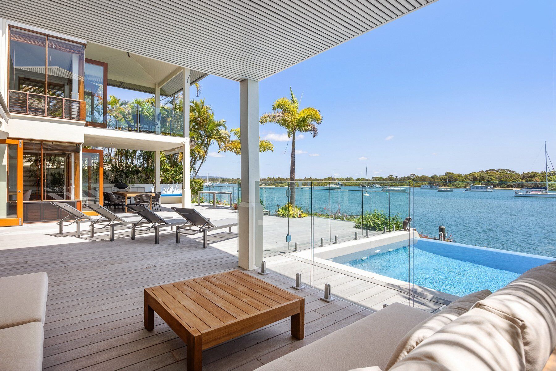 Eine moderne Außenterrasse mit Pool, Liegestühlen und einem Holztisch.