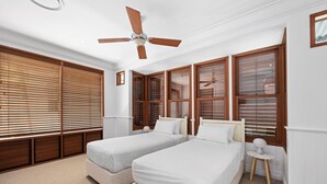 A bedroom with two beds, wooden blinds, a ceiling fan, and a small bedside table. - Riverside Elegance on Noosa Parade (Noosa)