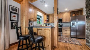 A kitchen with wooden cabinets, a stainless steel refrigerator, and two black bar stools. - Tranquil home near W&L, VMI (Lexington)