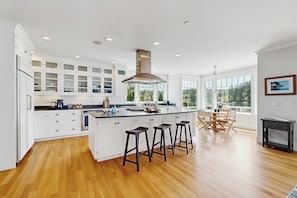 Une cuisine moderne avec des meubles blancs, un îlot central doté de tabourets et un coin repas avec une table et des chaises.