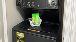 A compact, black coffee machine with a water dispenser and a basket for holding items.