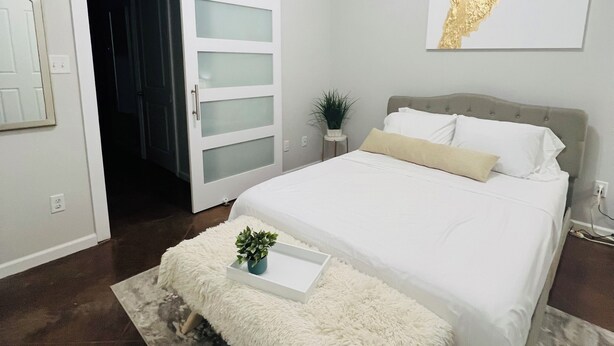 A bedroom with a bed, a ceiling fan, a sliding door, a wall-mounted artwork, and a small potted plant.