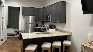 A modern kitchen with dark cabinets, stainless steel appliances, a granite countertop, and a bar area with stools.