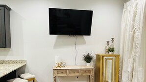 A kitchen with a TV mounted on the wall, a wooden console table, bar stools, and a cabinet.