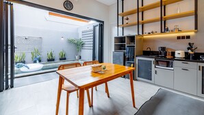 A modern kitchen with wooden cabinets, a built-in oven, and a microwave. There is a dining table with chairs and a potted plant. - Feels Like Home Villa (Blahbatuh)