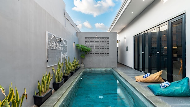 A modern outdoor pool area with a concrete wall, potted plants, and a sign that reads "FEELS HOME." - Feels Like Home Villa (Blahbatuh)