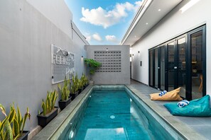 A modern outdoor pool area with a concrete wall, potted plants, and a sign that reads "FEELS HOME." - Feels Like Home Villa (Blahbatuh)