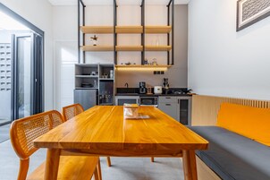 Una cocina moderna con una mesa y sillas de madera, horno empotrado y un sofá gris con un cojín naranja.