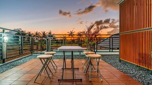 A wooden deck with a table and four chairs, surrounded by a metal railing and a wooden fence. - Feels Like Home Villa (Blahbatuh)