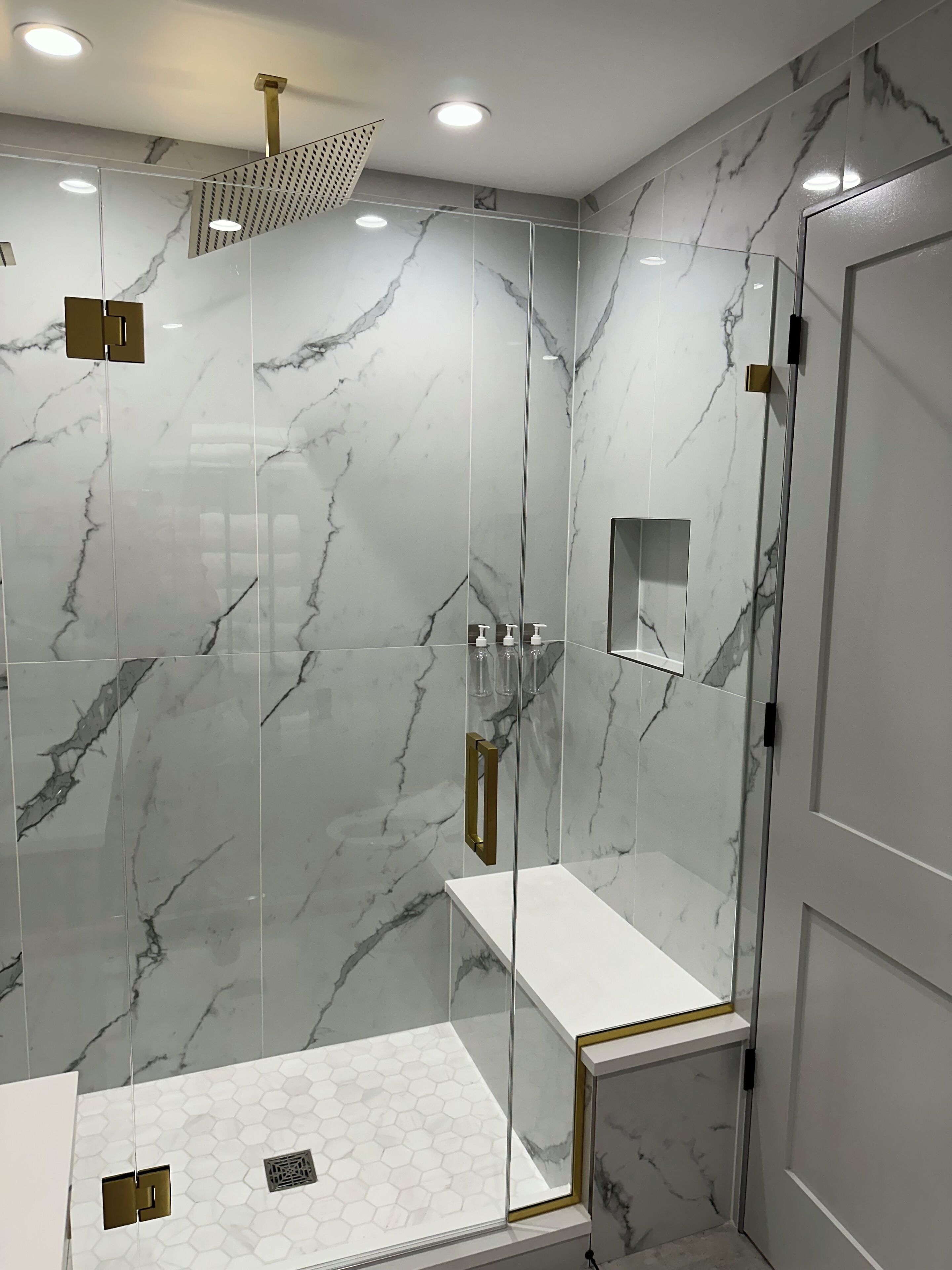 Une salle de bain moderne avec une douche à parois de verre, des murs en marbre et un sol recouvert de carreaux hexagonaux blancs.