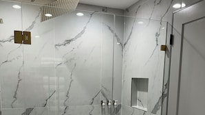 A modern bathroom with a glass-enclosed shower, marble walls, and a white hexagonal tile floor. - Exquisite Chicago Modern Rooftop, Sleeps 9 (Chicago)