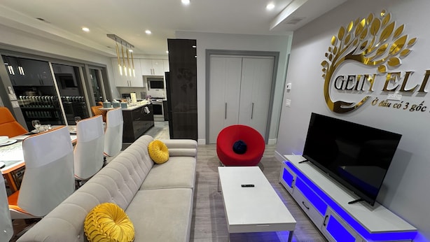 A modern living room with a sofa, a red chair, a TV, and a dining area in the background. - Exquisite Chicago Modern Rooftop, Sleeps 9 (Chicago)