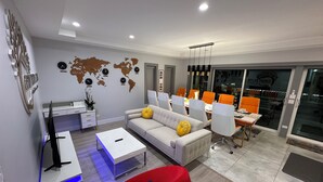 A modern living room with a sofa, a red chair, a dining area with orange chairs, a world map on the wall, and a desk with a computer. - Exquisite Chicago Modern Rooftop, Sleeps 9 (Chicago)