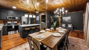 A modern kitchen with a wooden ceiling, stainless steel appliances, and a dining area with a wooden table set for six. - *Central! Game Room! Hot Tub!* (Pigeon Forge)