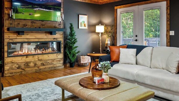 A cozy living room with a fireplace, a sofa, a coffee table, and a TV mounted on the wall. - *Central! Game Room! Hot Tub!* (Pigeon Forge)
