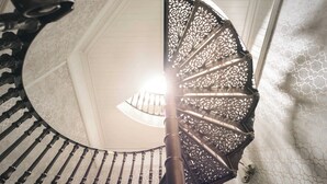A spiral staircase with ornate metal railings and a white wall with a geometric pattern. - High Cross Lodge | Ridgestone (Troutbeck)