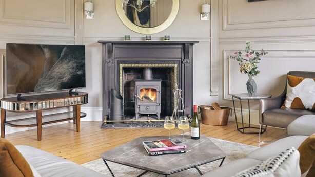 A living room with a fireplace, a television, a coffee table with books, and a sofa. - High Cross Lodge | Ridgestone (Troutbeck)