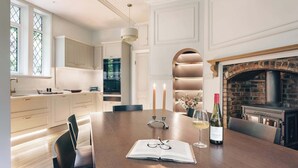 A dining area with a wooden table, two candles, a bottle of wine, and a book. - High Cross Lodge | Ridgestone (Troutbeck)