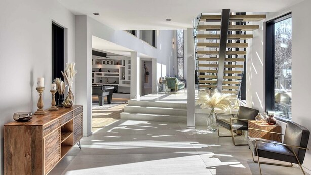 A modern interior with a staircase leading to a loft area, a pool table, and a seating area with a view of the outdoors.