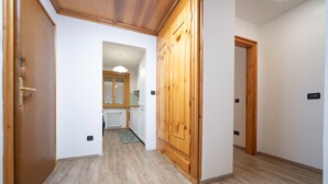 A hallway with wooden flooring, a wooden wardrobe, and a door leading to a kitchen area. - New apartment in the center of Canazei (Canazei)